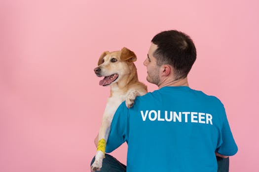 A cheerful volunteer holding a happy dog against a pink background.